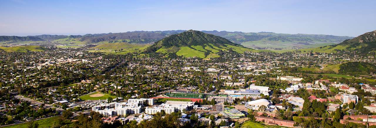 Aerial view of San Luis Obispo with Cal Poly’s campus in the foreground and green rolling hills and mountains in the background on a clear day.